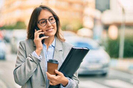 Young hispanic businesswoman talking on the smartphone and drinking take away coffee at the city.