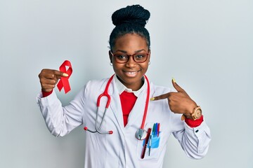 Young african american woman wearing doctor uniform holding support red ribbon pointing finger to...