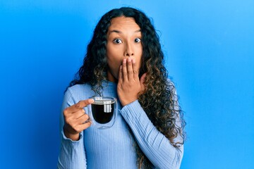 Young latin woman holding coffee covering mouth with hand, shocked and afraid for mistake. surprised expression