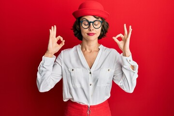 Young brunette woman wearing stewardess style and glasses relax and smiling with eyes closed doing meditation gesture with fingers. yoga concept.