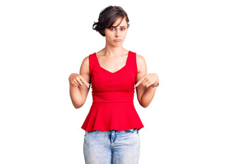 Beautiful young woman with short hair wearing casual style with sleeveless shirt pointing down looking sad and upset, indicating direction with fingers, unhappy and depressed.