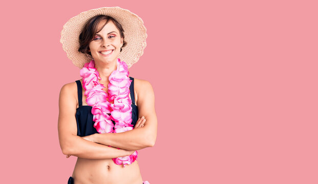 Beautiful young woman with short hair wearing bikini and hawaiian lei happy face smiling with crossed arms looking at the camera. positive person.