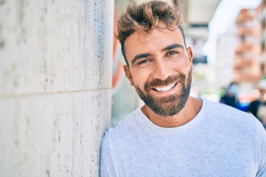 Young hispanic man smiling happy leaning on the wall at the city