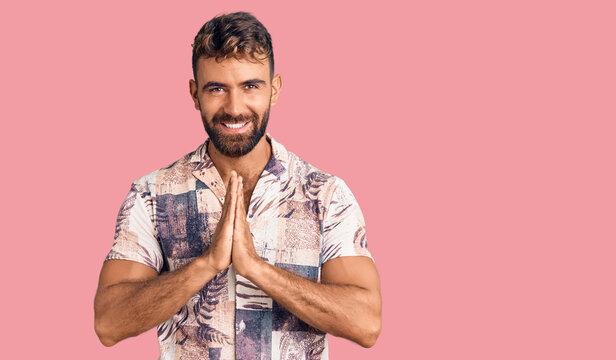 Young hispanic man wearing summer clothes praying with hands together asking for forgiveness smiling confident.