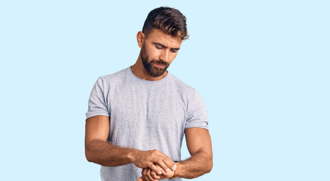 Young hispanic man wearing casual clothes checking the time on wrist watch, relaxed and confident