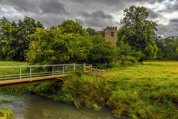 Fototapeta na wymiar A rural path leads across the fields and streams towards a Norman church near Wistow, UK in summertime