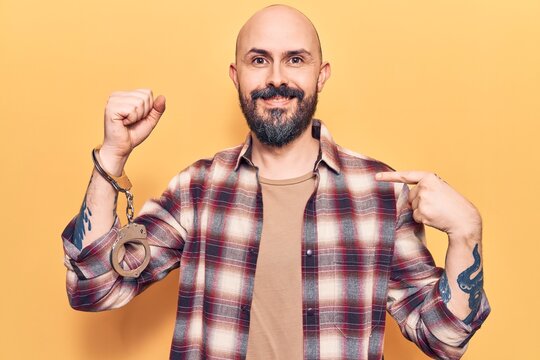 Young handsome man wearing prisoner handcuffs pointing finger to one self smiling happy and proud