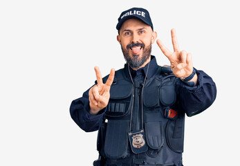 Young handsome man wearing police uniform smiling with tongue out showing fingers of both hands doing victory sign. number two.