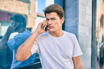 Young caucasian man with serious expression talking on the smartphone at the city.