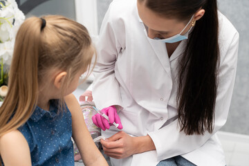 A nurse is getting ready to inject a little girl with a previously prepared vaccine. The young apprentice tries to talk to the child so that she is not afraid of the injection.