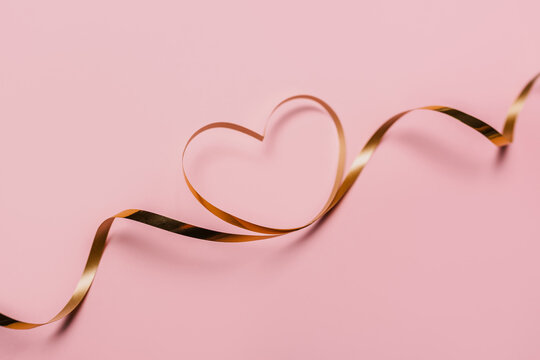 shape heart by gold ribbon on isolated pink background