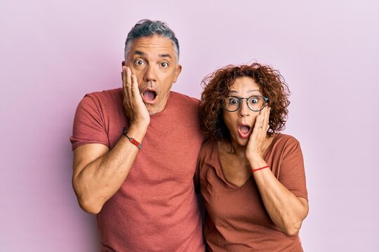 Beautiful middle age couple together wearing casual clothes afraid and shocked, surprise and amazed expression with hands on face