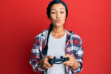 Beautiful hispanic woman playing video game holding controller looking at the camera blowing a kiss being lovely and sexy. love expression.