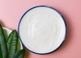 cosmetic cream in a blue jar with green leaves on a pink background. beauty, relaxation and face and body care concept
