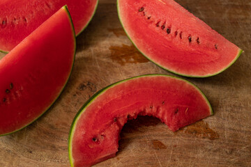 Slices of small watermelon with bite, on wooden board