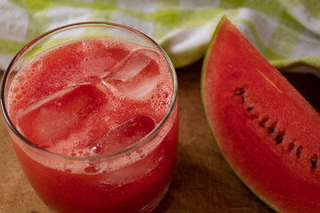 Tropical watermelon drink with ice cubes and fruit slices in the background