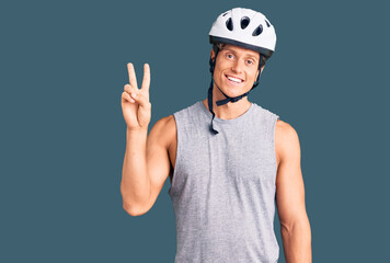 Young handsome man wearing bike helmet showing and pointing up with fingers number two while smiling confident and happy.