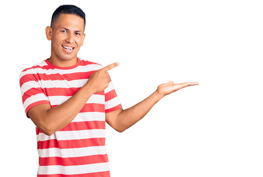 Young handsome latin man wearing casual clothes amazed and smiling to the camera while presenting with hand and pointing with finger.