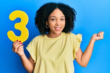 Young african american girl holding number three screaming proud, celebrating victory and success...