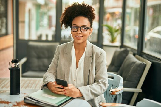 Young african american businesswoman smiling happy using smartphone sitting at coffee shop.