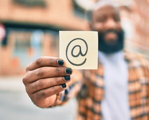 Handsome modern african american man with beard smiling positive standing at the street showing email symbol on paper