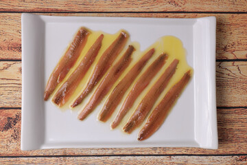 Portion of anchovies from Santoña, Cantabrian anchovies in white rectangular plate on wooden table