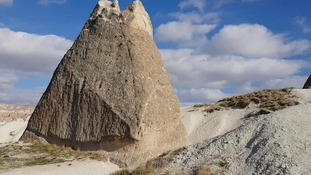 Cappadocia landscape with fairy chimney rock formations and white sandy desert under blue sky with white clouds. Panning view of volcanic mountains and caves of Kapadokya Turkey