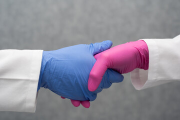 Two people from the healthcare industry shake hands from two different labs as a sign of working...