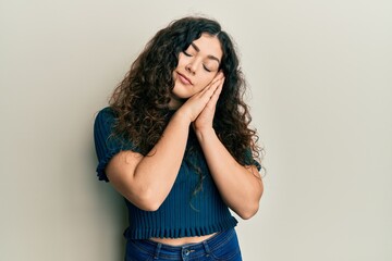 Young brunette woman with curly hair wearing casual clothes sleeping tired dreaming and posing with hands together while smiling with closed eyes.