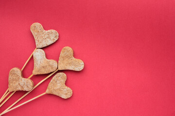 Heart shaped cookies on a stick on a red background. Valentines treats on colored backdrop. Flat lay, copy space