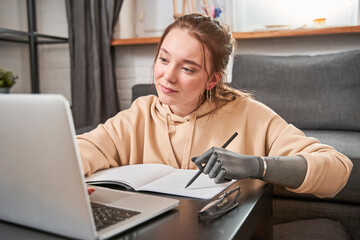 Woman with prosthesis arm writing at notebook