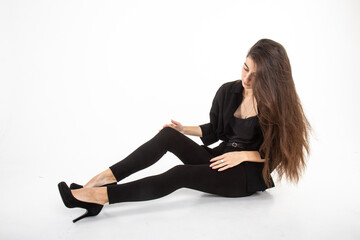 Fototapeta premium Attractive young woman with long brown hair in black clothes sitting on white background. Vertical view. Copy space