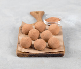 Energy balls made of dates, almonds and cocoa on a wooden board on a light gray background