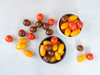 Red, orange, yellow grape tomatoes on white background. Large cherry tomatoes in white and brown bowls.