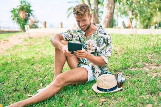Caucasian handsome man smiling happy using touchpad device sitting on the grass at the park