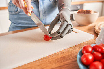 Woman with prosthesis arm is cutting ingredients on table