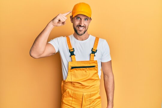 Young handsome man wearing handyman uniform over yellow background smiling pointing to head with one finger, great idea or thought, good memory