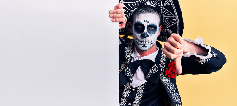 Young Man Wearing Mexican Day Of The Dead Costume Holding Blank Empty Banner With Angry Face, Negative Sign Showing Dislike With Thumbs Down, Rejection Concept