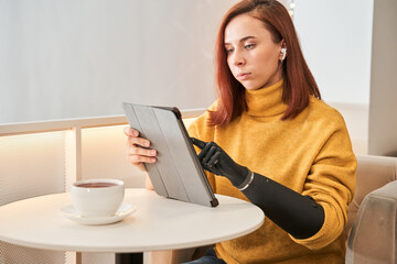 Woman with prosthesis arm using digital tablet at table in cafe