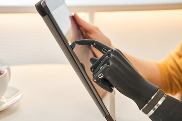Woman with prosthesis arm typing on digital tablet