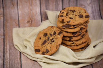 Stack of freshly baked chocolate chip cookies on a towel with wooden backdrop