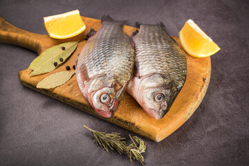 Fish Carp not peeled on a cutting board with lemon and spices on a gray mottled background