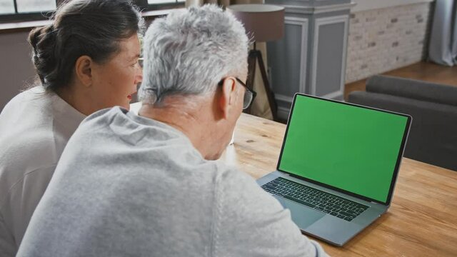 Back view of aged couple looking at green screen of laptop and talking to someone using online video call, Chroma key