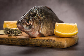 Fish Carp not peeled on a cutting board with lemon and spices on a gray mottled background