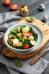 light spring salad with spinach, eggs, mushrooms and tomato, salad in a gray plate on a wooden board