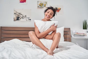 Foto op Canvas Girl sitting in bed and hugging pillow while smiling © Yakobchuk Olena
