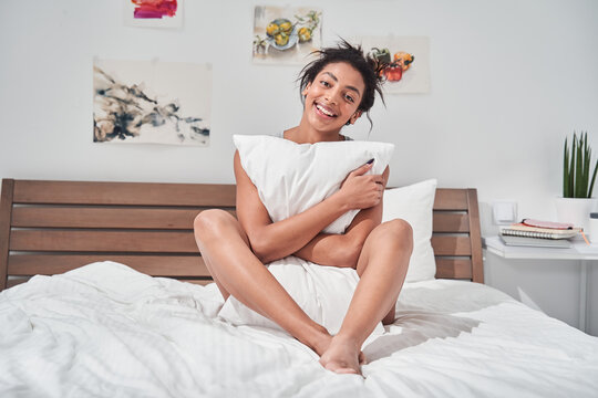 Girl sitting in bed and hugging pillow while smiling