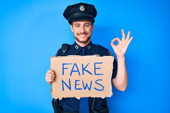 Young caucasian man wearing police uniform holding fake news banner doing ok sign with fingers, smiling friendly gesturing excellent symbol
