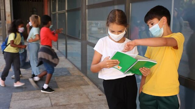 Portrait of primary school girl and boy wearing protective face masks talking outside before lesson, new normal during coronavirus pandemic situation