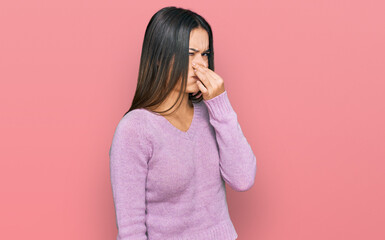 Young hispanic girl wearing casual clothes smelling something stinky and disgusting, intolerable smell, holding breath with fingers on nose. bad smell